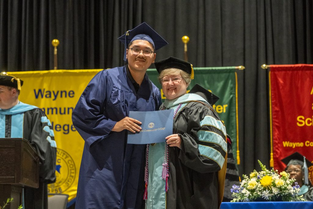 A man and woman stand beside each other in graduation caps and gowns.