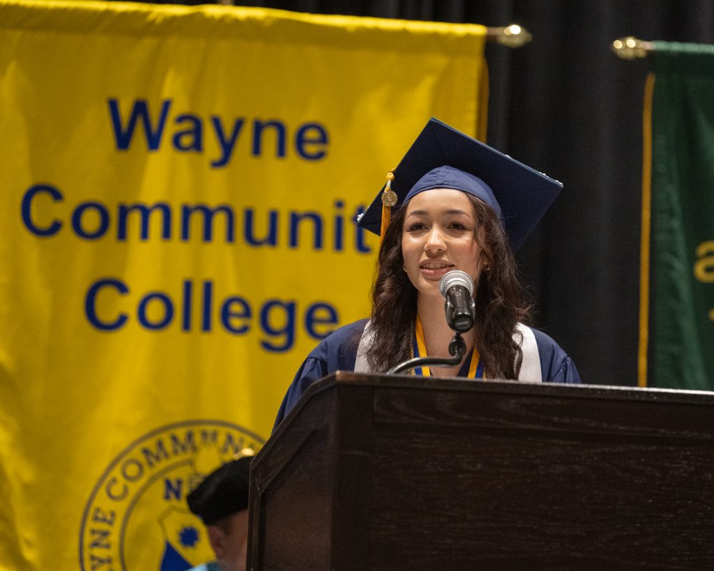 A graduate speaks into a microphone at a podium while wearing a cap and gown.