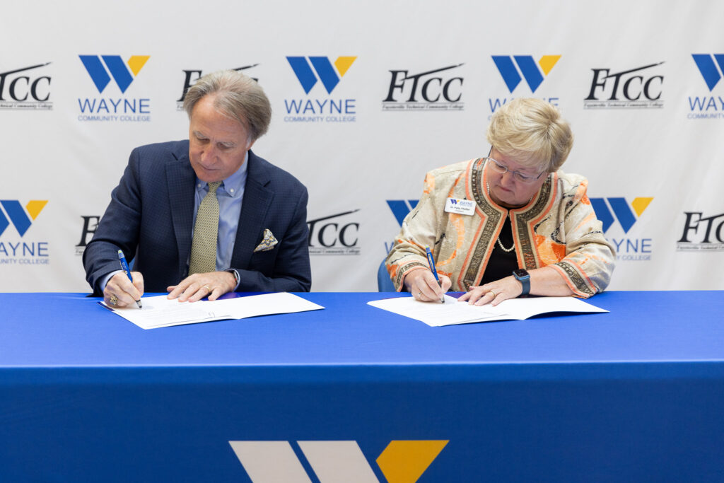 A man and woman sign documents while sitting at a table.