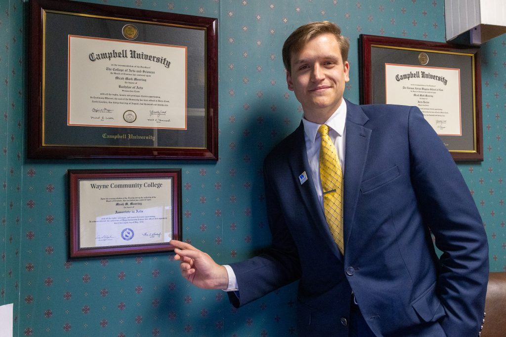 A man points to his diploma hanging on the wall. 