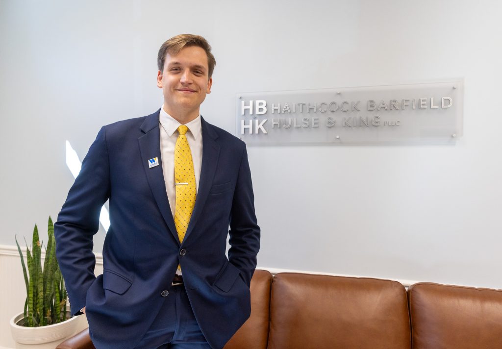 A man stands next to a sign displaying the name of a law firm.