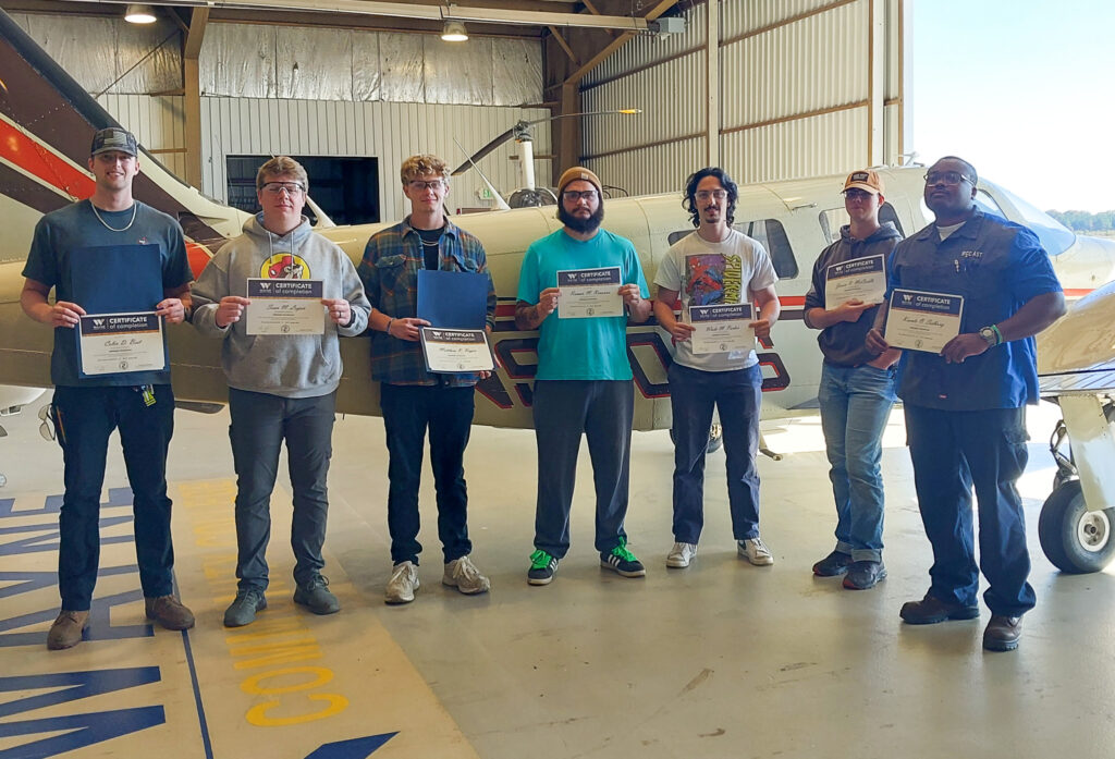 Individuals stand next to an airplane while holding certificates.