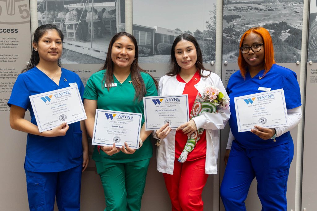 Graduates hold certificates for a photo while wearing medical scrubs.