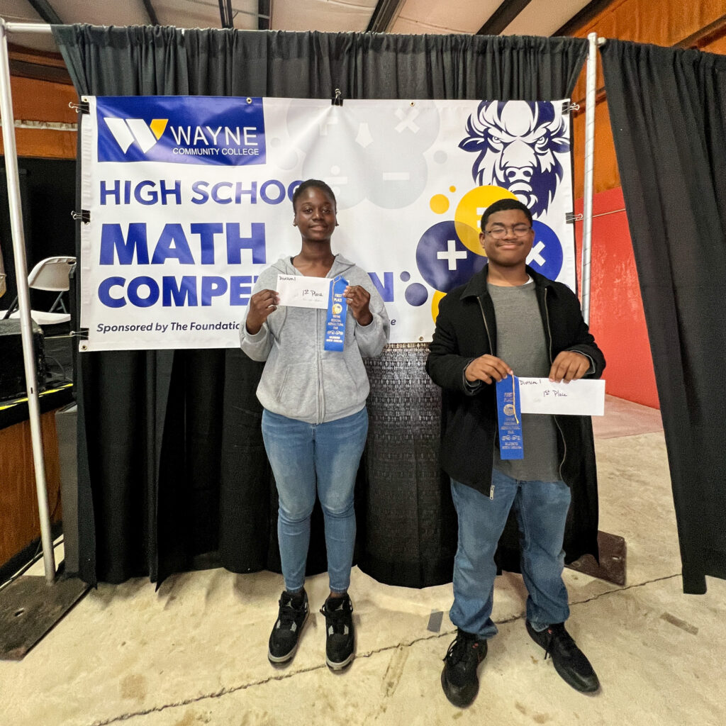 Two students stand holding blue ribbons and envelopes.