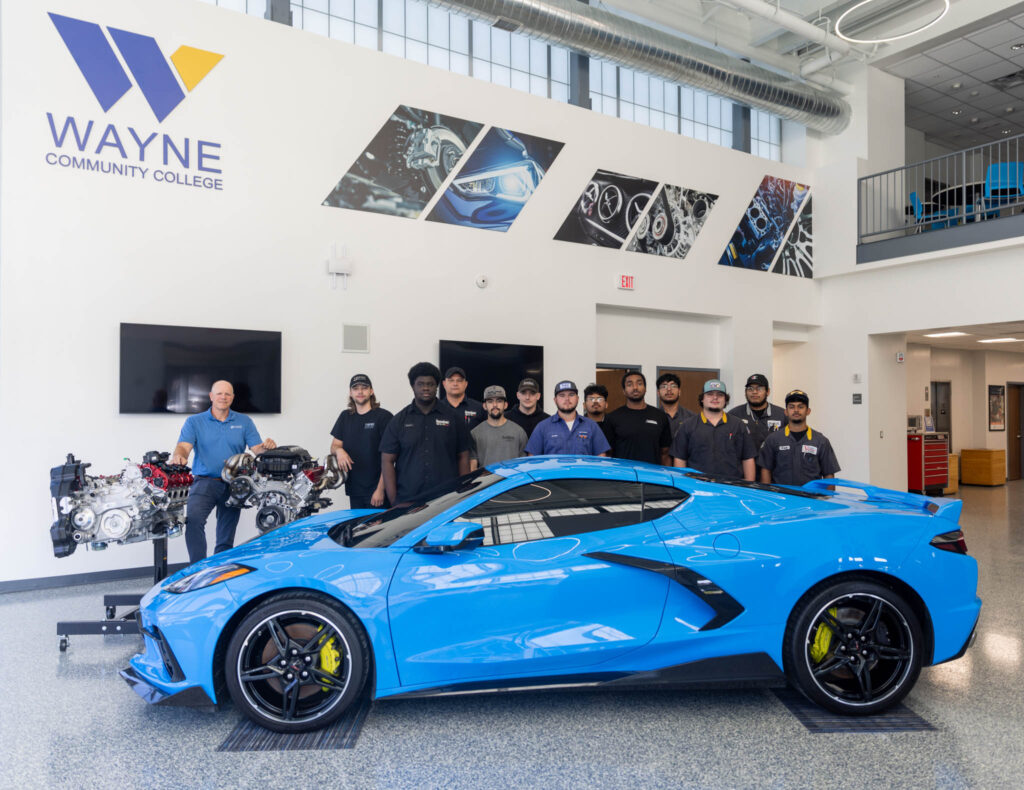 Individuals stand around a blue car.