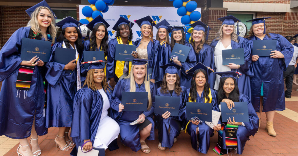 A group of women in caps and gowns hold their diplomas.