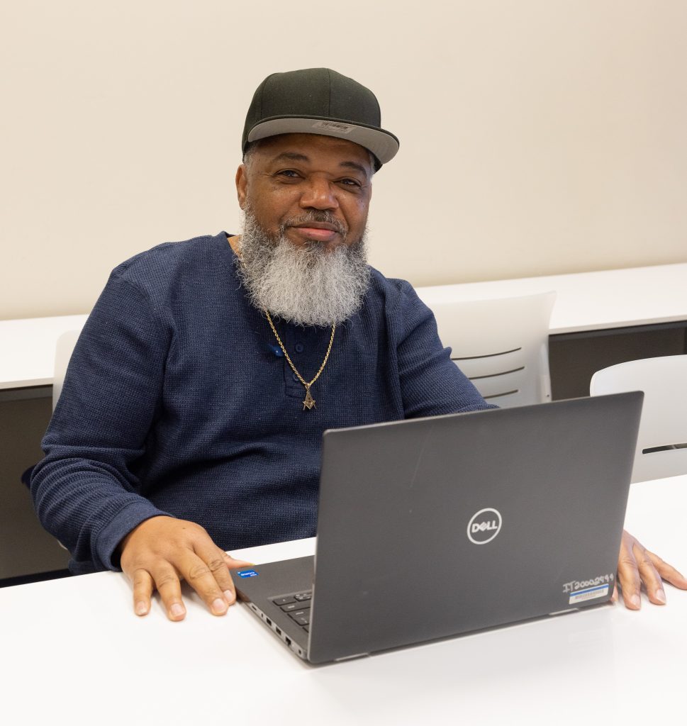 A man sits at a desk with an open laptop in front of him.