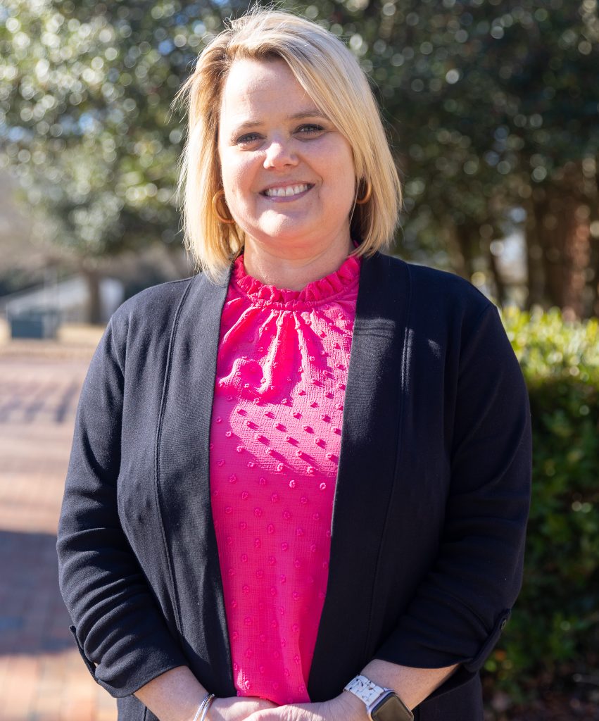 A woman wearing a pink shirt and black sweater smiles for the photo. 