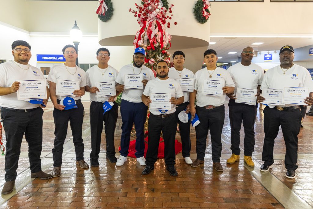 A group of people stand together holding certificates and hats.