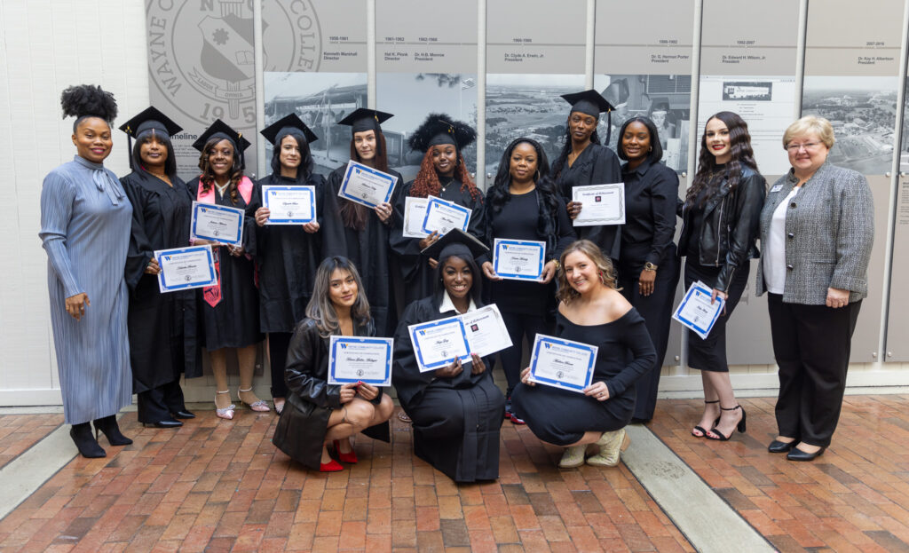 Graduates stand with their certificates while wearing caps and gowns.