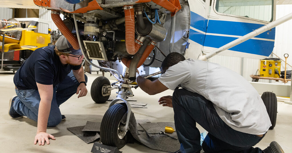 Two men perform mechanic work on an airplane.