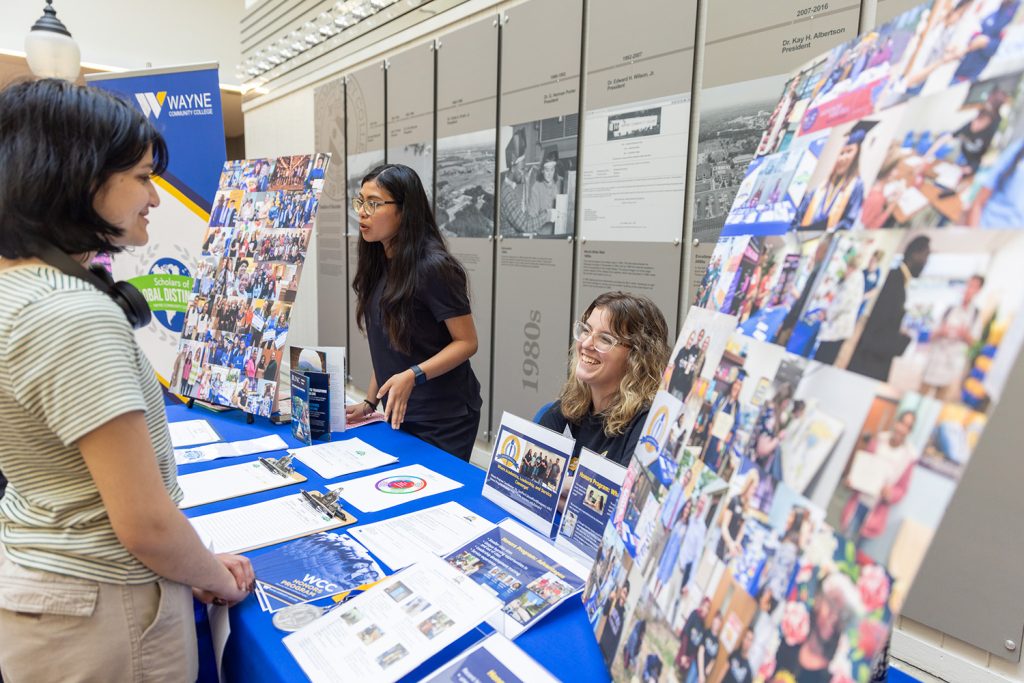 Three individuals stand around a table displayed with photos and information.