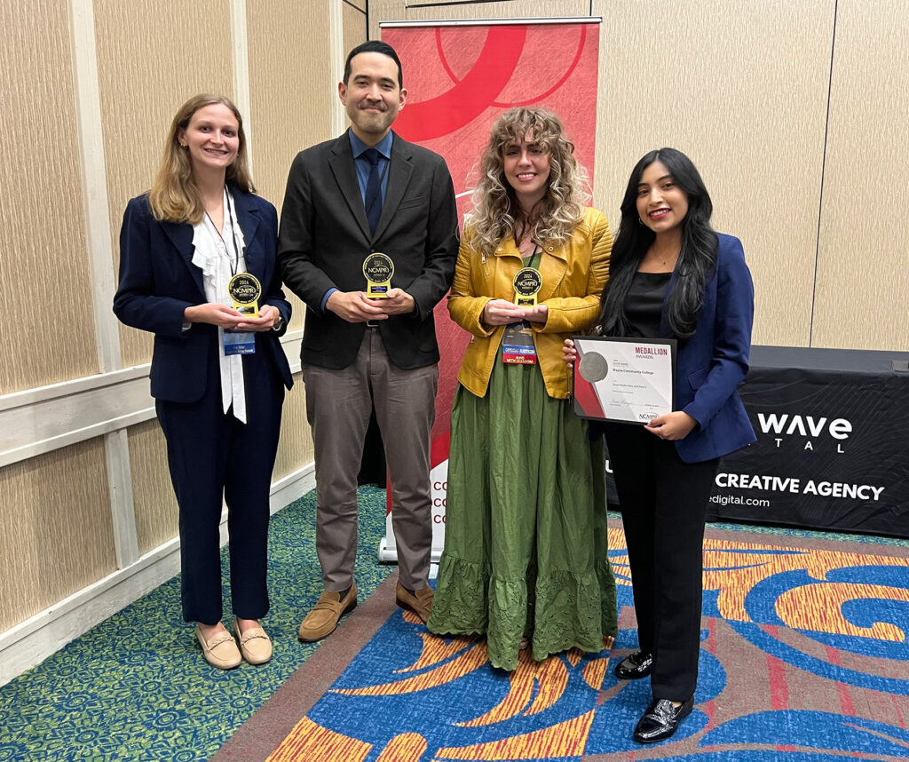 Four people stand and hold awards.